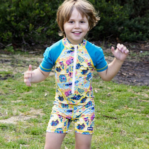 little-boy-standing-with-short-sleeve-sun-safe-yellow-and-blue-swimsuit