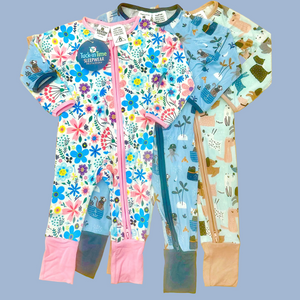 Two children's onesies with floral and animal patterns on a wooden surface