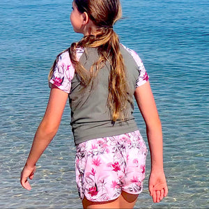 Girl in a swimsuit standing in shallow water with a clear blue background