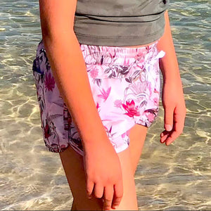 Young girl in a floral swimsuit standing in clear water at the beach