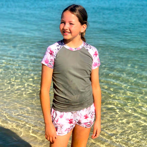 Young girl standing in clear water wearing a floral shirt and shorts with a gray sleeve.