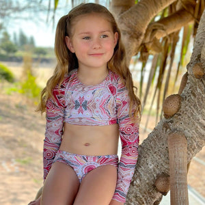 Young girl in a colorful swimsuit sitting on a tree branch with a natural background