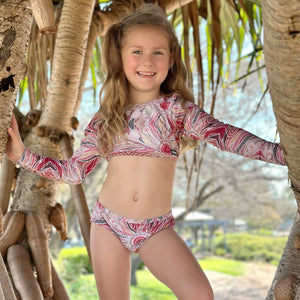 Young girl in a pink and white patterned swimsuit standing between palm trees.