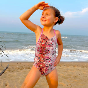 Young girl in a patterned swimsuit standing on a beach with ocean in the background