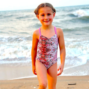Young girl in a swimsuit standing on a sandy beach with ocean waves in the background