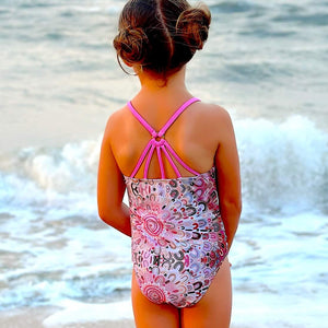 Child in a swimsuit standing on a beach with ocean waves in the background