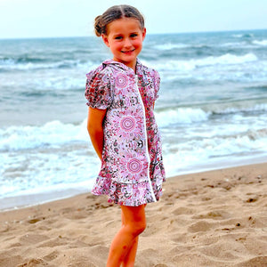 Young girl in a pink dress standing on a sandy beach with ocean waves in the background