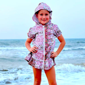 Child wearing a pink hooded outfit on a beach with ocean waves in the background