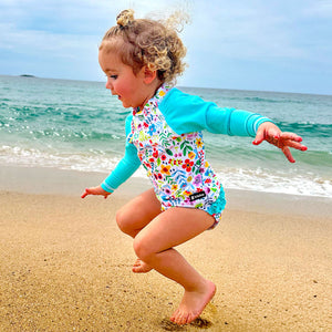 Child in a colorful swimsuit playing on a sandy beach with ocean in the background