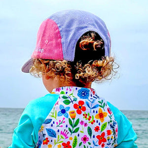 Child in colorful swimsuit and hat standing on a beach with ocean view