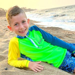 Child in colorful swimwear lying on a sandy beach with ocean in the background