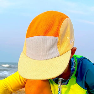 Child playing in the sand on a beach with a colorful hat and swimsuit.