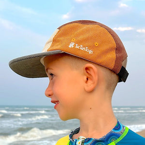 Child wearing a bright green and blue shirt with a cap on a beach