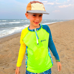 Child wearing a bright yellow and blue shirt with a cap on a beach