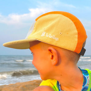 Child wearing a bright yellow cap and colorful swimsuit on a beach