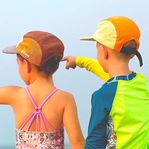 Two children in swimsuits standing on a beach, pointing towards the ocean.