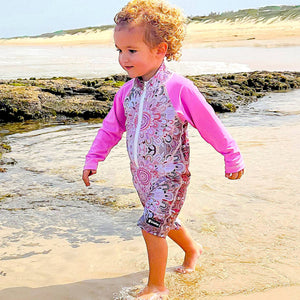 Child in a colorful swimsuit walking on a sandy beach with ocean and sky in the background