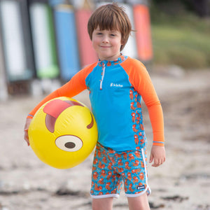 Little-boy-standing-in-orange-and-blue-octopus-two-piece-swimwear-set